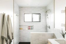 a modern bathroom with marble skinny tiles and black ones on the floor, a floating wooden vanity, a built-in niche for storage
