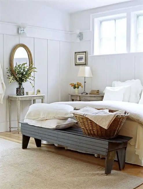 a neutral Provence bedroom with weathered wood nightstands, a refined vanity, a dark bench and a basket