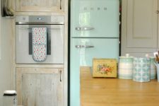 a neutral and pastel vintage kitchen with a blue fridge, a green bench, colorful mosaic tiles on the floor, a large kitchen island