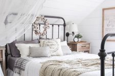 a neutral attic bedroom with a vintage and farmhouse feel, a metal bed, neutral and printed bedding, lace curtains and greenery
