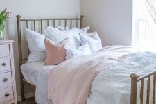 a neutral bedroom with a metal bed, a crystal chandelier, a blush sideboard and blush and white bedding