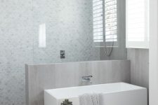 a neutral contemporary bathroom with marble fish scale tiles and a half wall covered with neutral wood plus the same on the floor