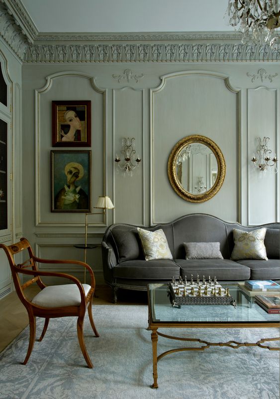 a neutral living room with elegant and refined paneling, a grey sofa, neutral chairs, a glass coffee table and some lovely artwork