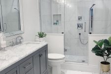 a neutral modern bathroom clad with marble hex tiles, with a shower space with half walls, a grey vnaity and a large mirror