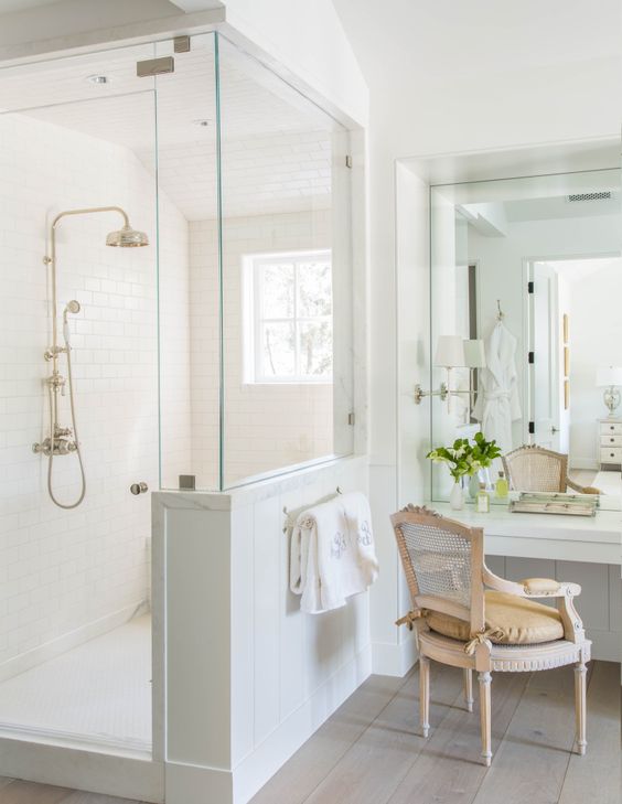 a neutral vintage bathroom with a shower space with a half wall, a vanity with a mirror and a vintage chair