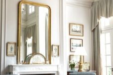 a neutral vintage living room with paneled walls, a fireplace, blue chairs, ottomans and stools, artworks and a large mirror