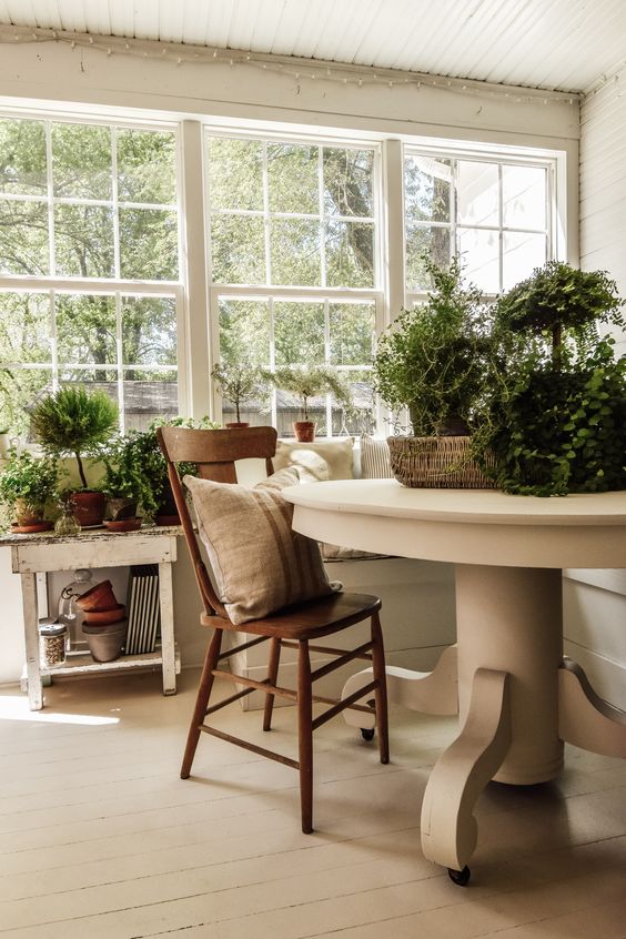 a neutral vintage sunroom with a stained chair, potted greenery and neutral textiles for a chic feel