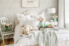 a pastel vintage bedroom with a printed wallpaper wall, a refined bed and nightstands, printed bedding and a crystal chandelier