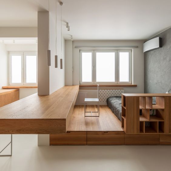 a plywood platform with drawers and shelves spearates the bedroom from the rest of the space, and an additional platform features a desk space