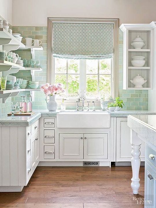 a pretty vintage cottage kitchen with white shaker style cabients, a green subway tile backsplash, open shelves and open cabinets and a printed curtain