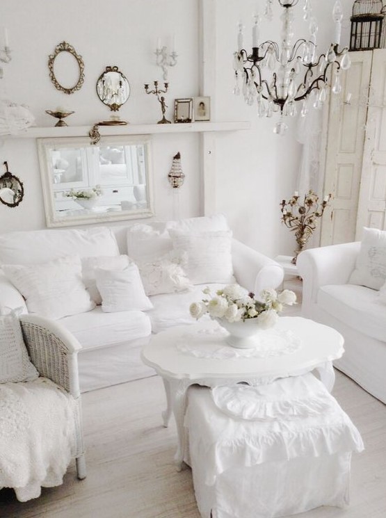 a pure white vintage living room with seating furniture, a woven chair, a carved coffee table, a crystal chandelier and a gallery wall of mirrors