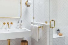 a refined bathroom with a dark floor, a shower space with a pony wall, white herringbone tiles and gold touches here and there
