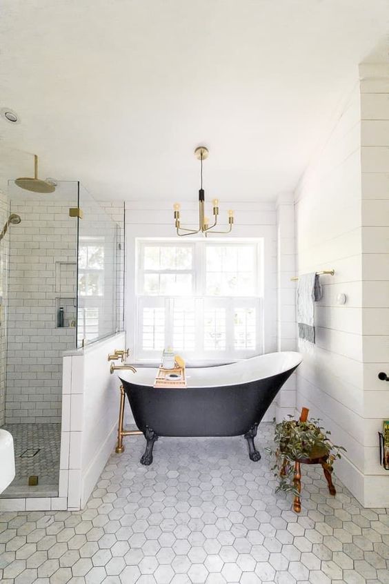 a refined farmhouse bathroom clad with hex and subway tiles, with a vintage bathtub, a stool with a plant and a vintage chandelier