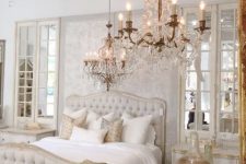 a refined neutral bedroom with a chic bed, crystal chandeliers, mirrors and printed pillows
