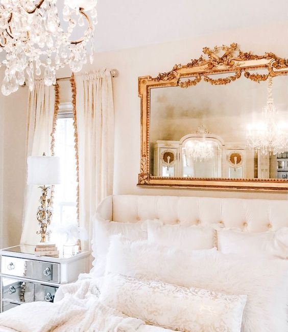 a refined neutral bedroom with a mirror in a chic frame, a crystal chandelier and a gorgeous upholstered bed