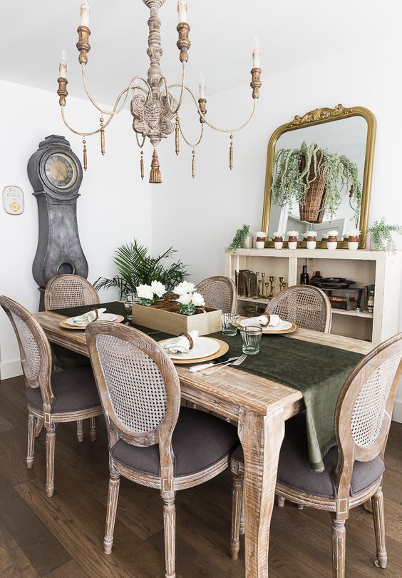 a refined rustic vintage dining room with a credenza, a large mirror, lots of greenery and an elegant stained dining set plus a vintage chandelier