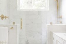 a refined white marble bathroom with half walls int he shower space and touches of gold for a more chic look