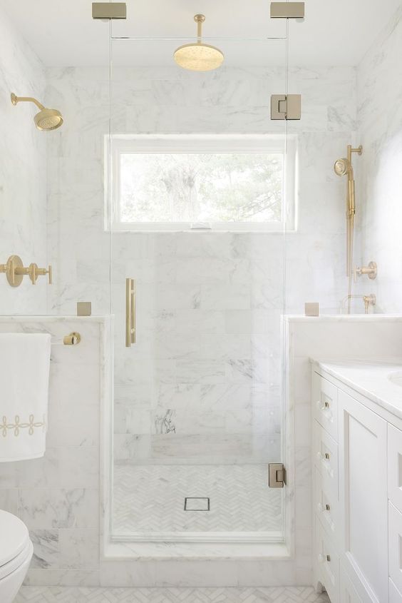 a refined white marble bathroom with half walls int he shower space and touches of gold for a more chic look