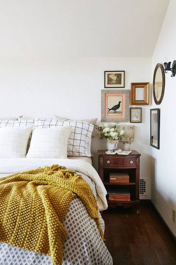 a retro bedroom with neutral walls, heavy and dark furniture, a gallery wall and white blooms is very chic