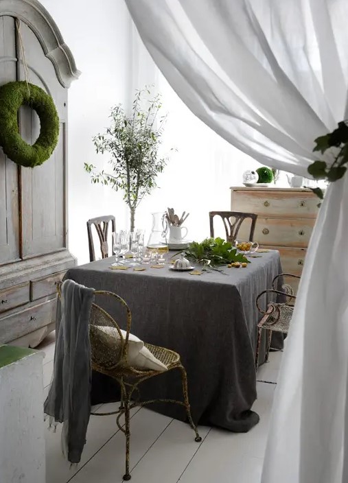a shabby chic meets Scandinavian dining room with neutral and dark linens, shabby chic furniture and some greenery and moss to refresh the space