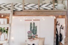 a small boho space with a pallet seat with pillows and a rug, guitars on the wall and string lights, a loft bed with a pendant bulb