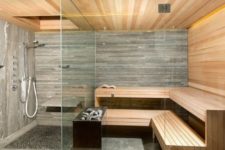 a small but very chic steam room clad with wood – light-stained and weathered and tiles plus built-in lights and glass walls