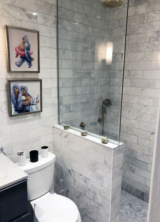 a small neutral bathroom with marble tiles, a shower space with a half wall, a small and fun gallery wall