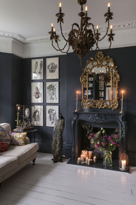 a sophisticated black living room with a beautiful fireplace, a mirror in a chic gold frame, a neutral sofa, bold blooms, candles and artwork