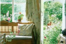 a stylish vintage rustic sunroom with wooden furniture, floral and other print textiles, potted blooms and greenery