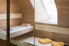 a tiny home steam room clad with light stained wood and a couple of benches plus a small window for natural light