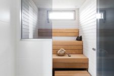 a tiny yet chic steam room clad with light stained and white wood, with step benches and a small skylight