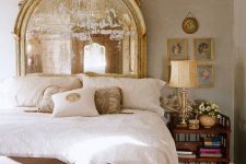 a vintage bedroom with neutral walls, a vintage mirror as a headboard, a crystal chandelier and a chic gallery wall
