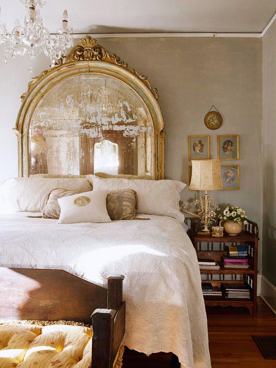 a vintage bedroom with neutral walls, a vintage mirror as a headboard, a crystal chandelier and a chic gallery wall