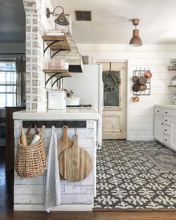 a vintage cottage kitchen in neutrals, with planked cabinets, stained shelves, a mosaic tile floor, metal pendant lamps and pans
