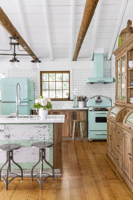 a vintage kitchen with stained cabinets, mint green appliances, a shabby chic kitchen island with green touches, wooden beams and vintage lamps