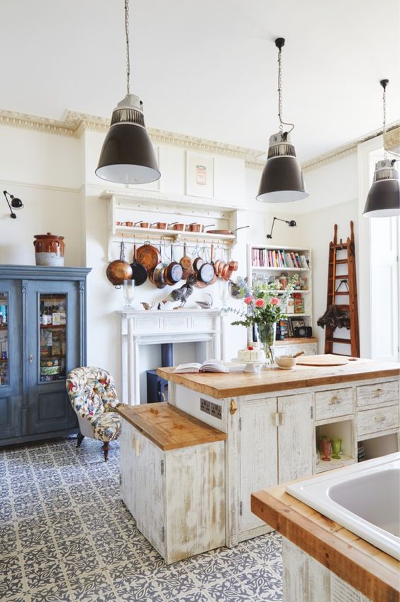 a vintage kitchen with white shabby chic cabinets, butcherblock countertops, black pendant lamps, a blue buffet and a vintage hearth