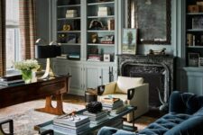 a vintage living room with blue walls, built-in storage units, a navy sofa, a tiered coffee table, a fireplace and a stained desk