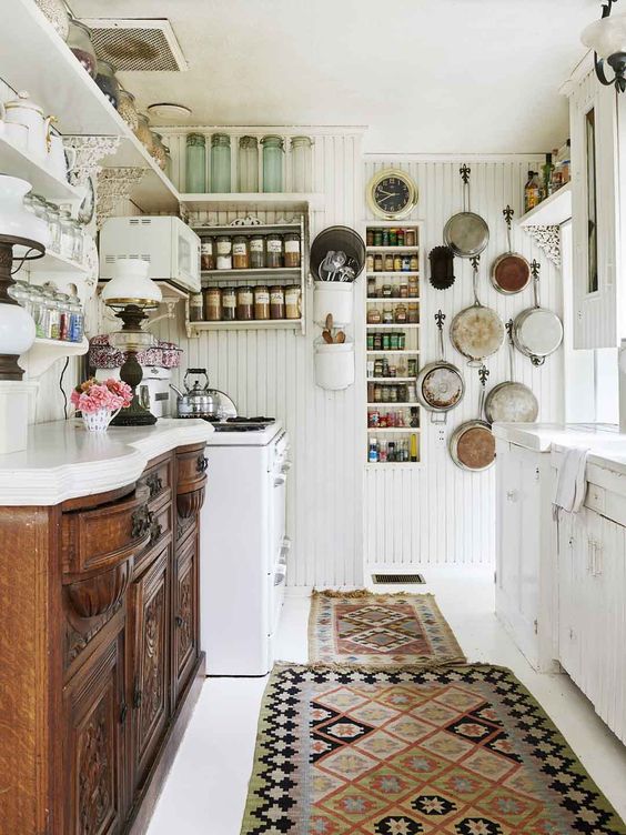 a vintage white kitchen with a stained buffet as cabinetry, white cabinets, white beadboard walls, open shelves and vintage pans for decor