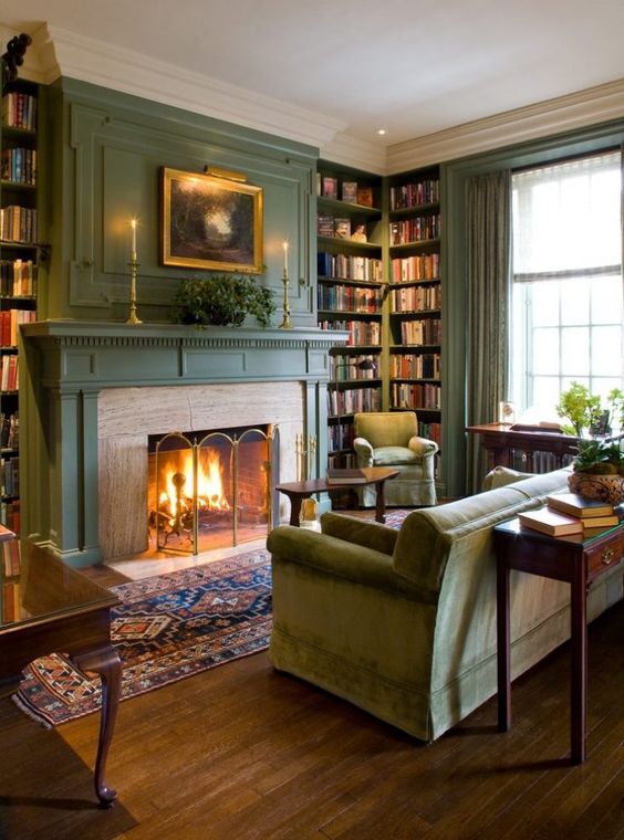 a welcoming vintage living room with green walls, a fireplace, built-in bookshelves, a green sofa and chairs, console tables