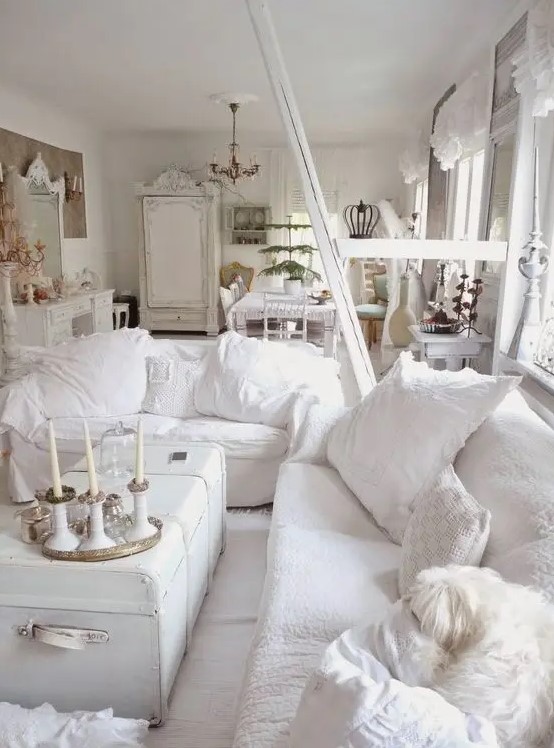 a white shabby chic living room with chic furniture, a white chest, white pillows and candles is very elegant