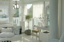 a white shabby chic living room with skylights, elegant white furniture, a crystal chandelier, a potted plant and greenery