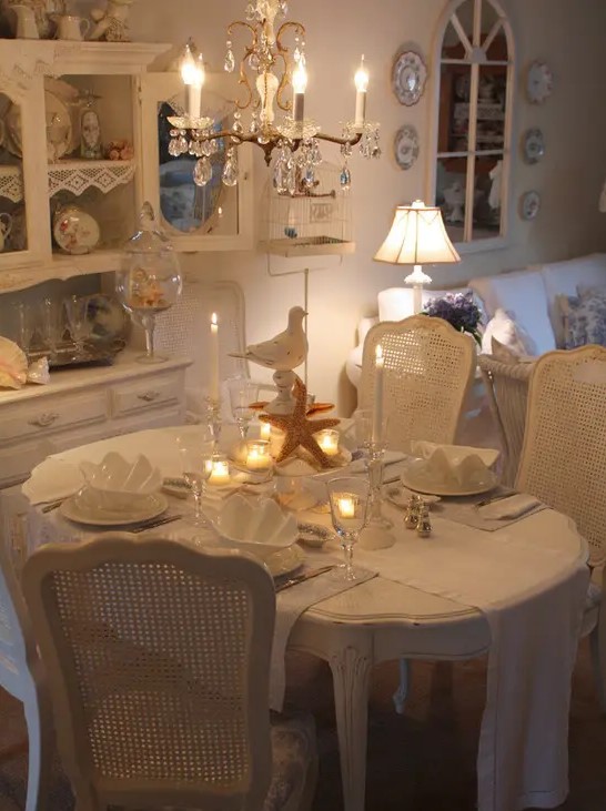 a white vintage dining room with elegant furniture, a crystal chandelier, some porcelain and glass and a cool lamp