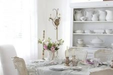 an elegant and neutral vintage dining room with a ruffle tablecloth, a crystal chandelier, shabby chic chairs and stylish porcelain