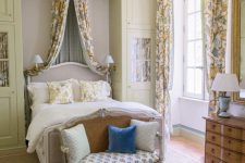 an exquisite Provence bedroom with tan cabinets, a grey bed with a refined design, floral textiles, a loveseat with pillows and lamps