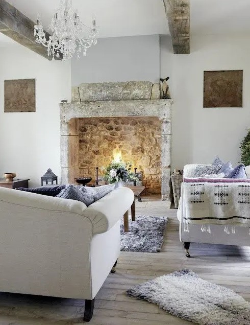 an exquisite Provence living room with a stone fireplace, refined furniture, a crystal chandelier and wooden beams, white and blue textiles