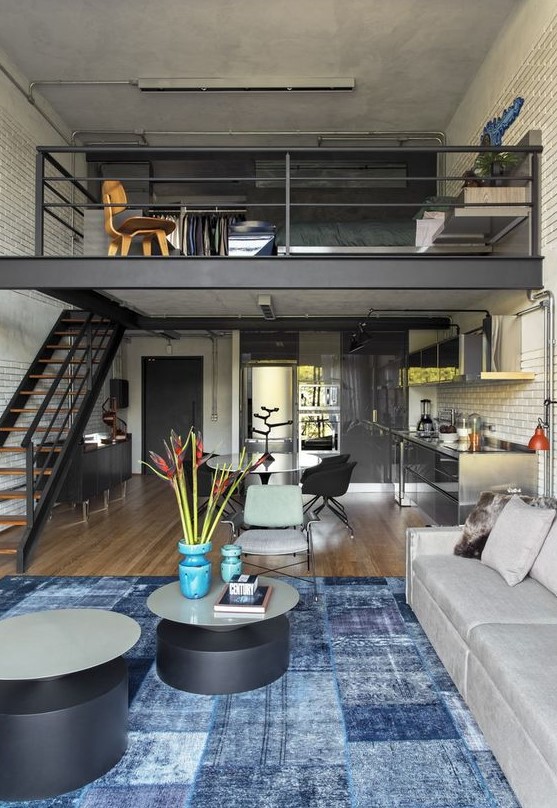 an industrial home with a loft sleeping space and closet, with a dining-living room below and round tables is a stylish idea