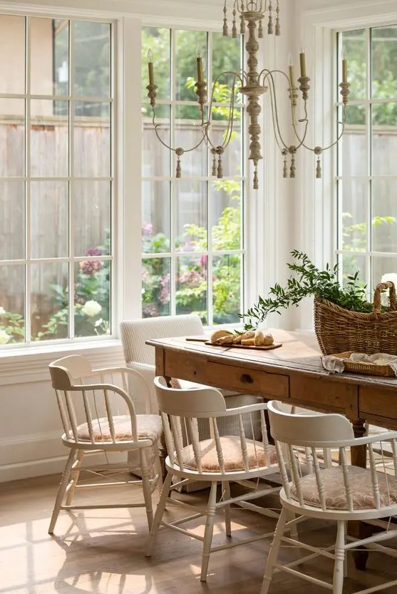 a French cottage dining room with a stained table, vintage white chairs, a chic chandelier and a basket with greenery