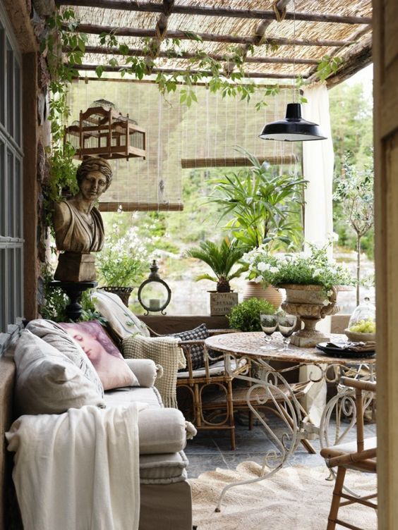 a Provence-inspired terrace with rattan and metal furniture, neutral and pastel textiles, potted greenery and blooms and some pendant lamps