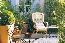 a Provence terrace with a woven chair, a metal table and some chairs, potted greenery and blooms and lots of sunlight