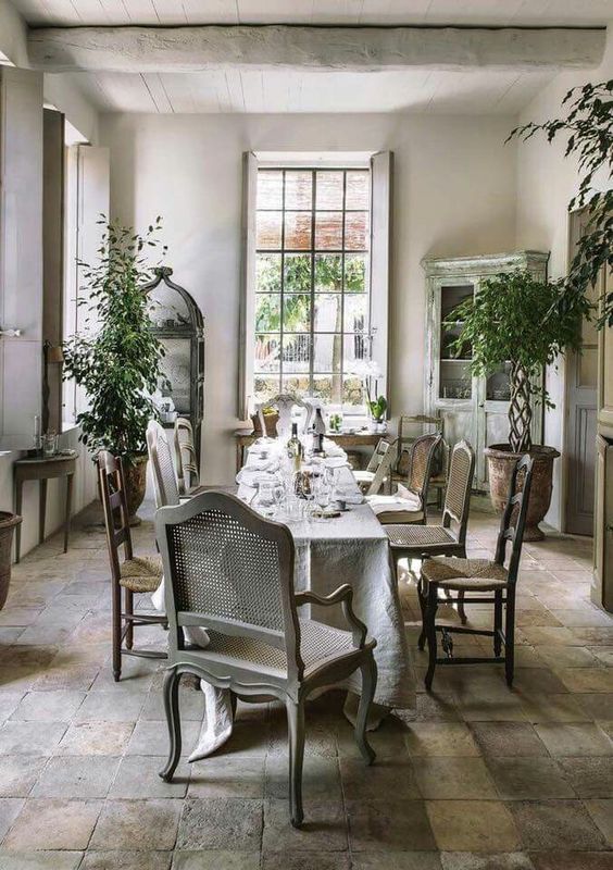 a beautiful Provence dining room with a couple of vintage buffets, a long table, vintage chairs, potted trees and lots of light